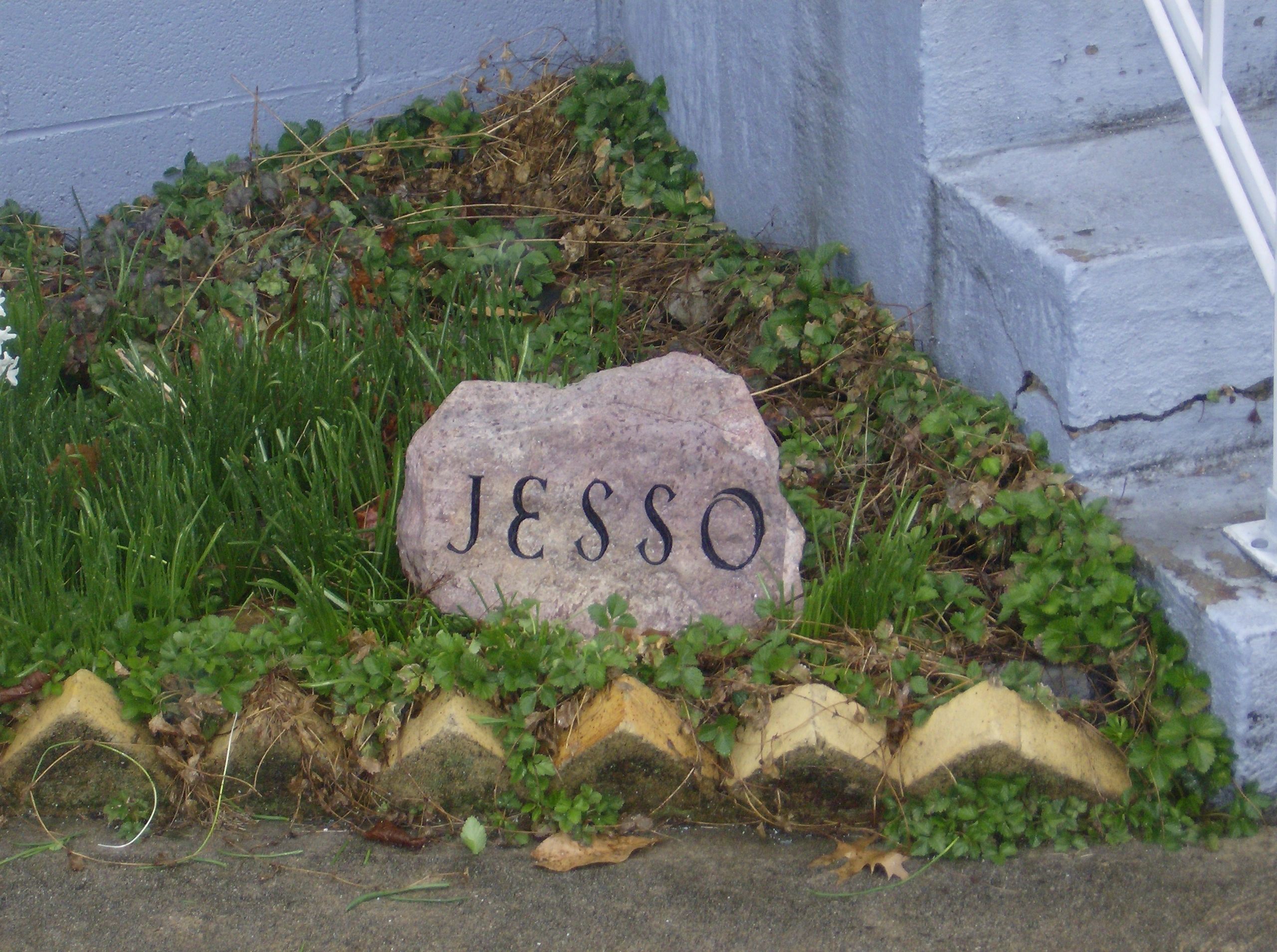 A natural boulder carved with the name Jesso, set into the planting beside the workshop steps