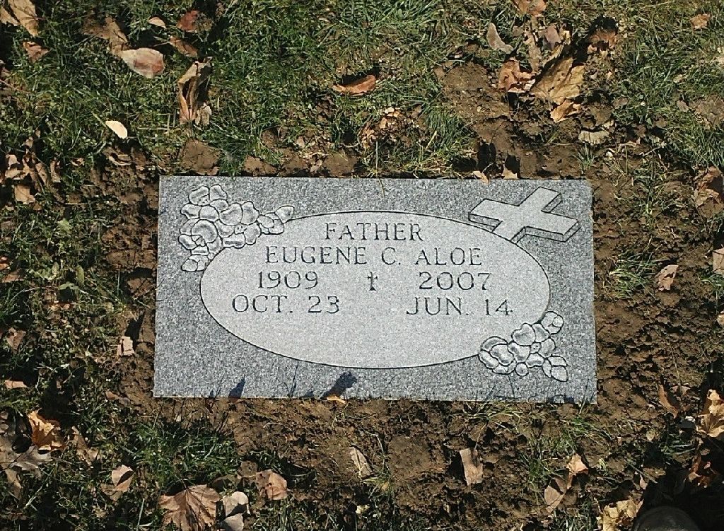 Grey flush marker with a carved cross and flowers, autumn leaves around it