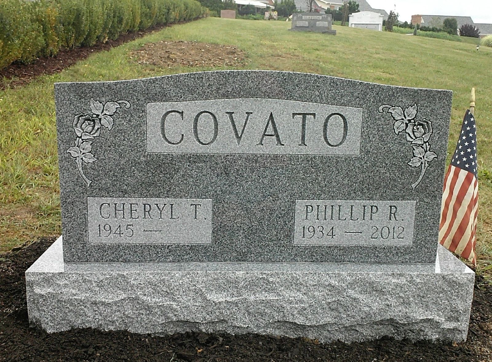 Grey granite double upright monument with carved roses on both shoulders and a rock pitched base