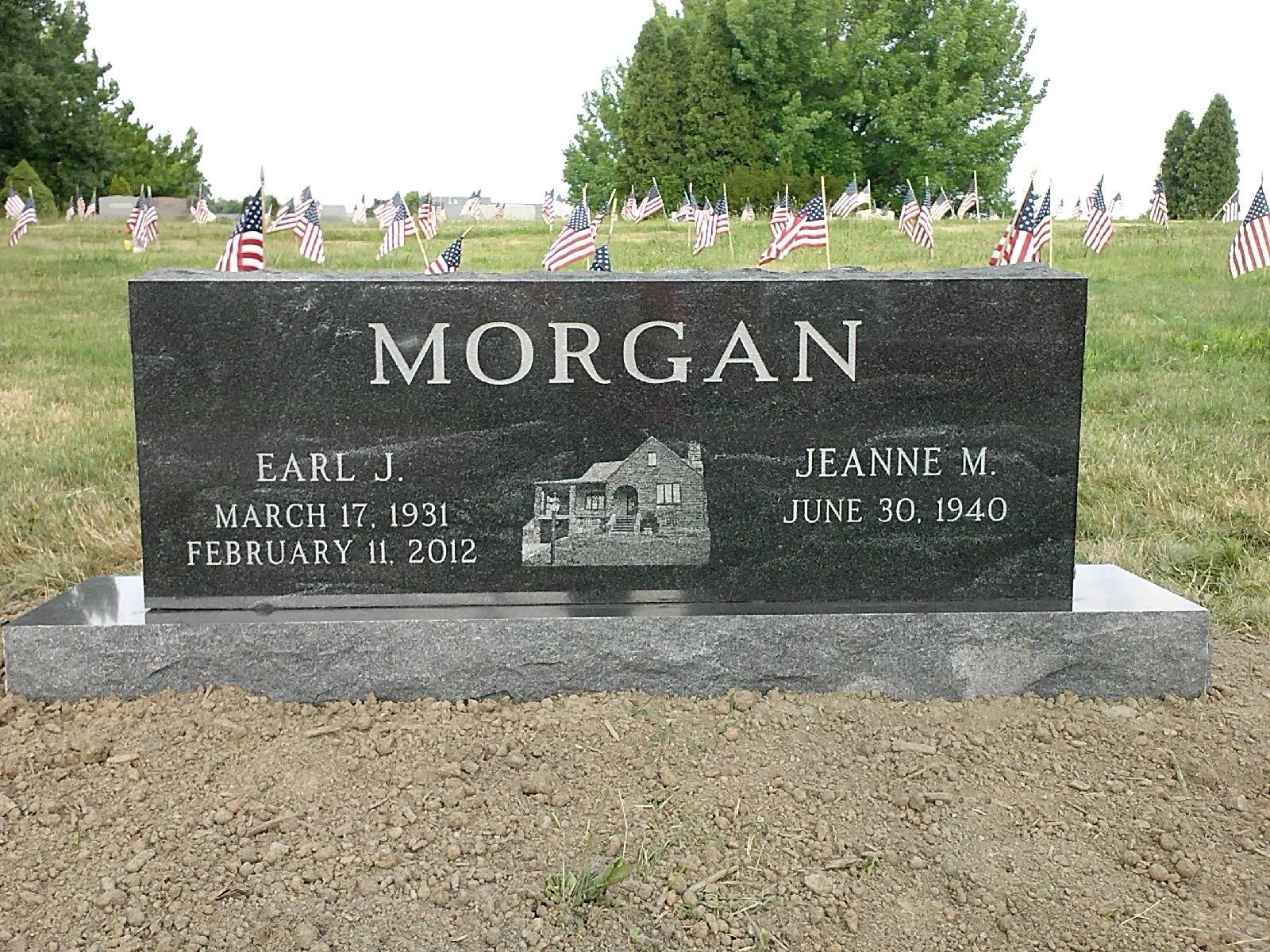 Black granite double upright with an etched house scene, in a cemetery lined with flags