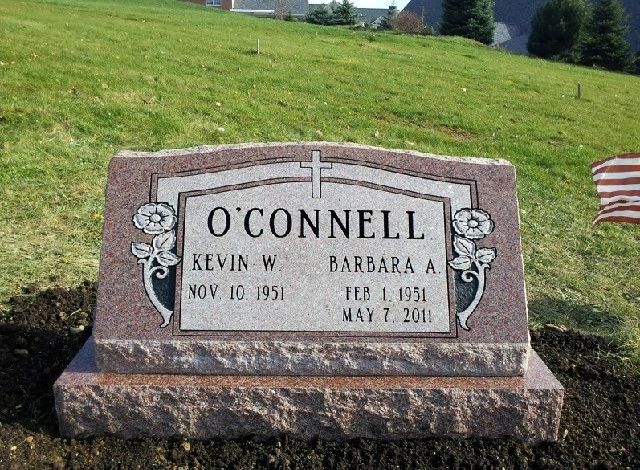 Red granite upright monument with a carved scroll panel and cross