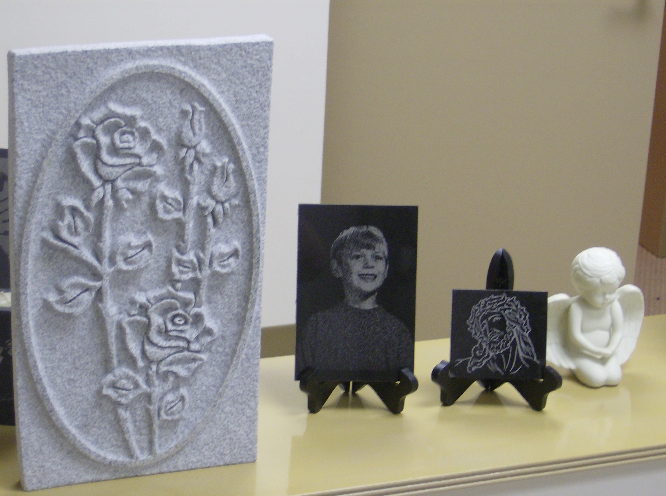 A hand carved rose relief panel in granite beside portrait etchings displayed on easels